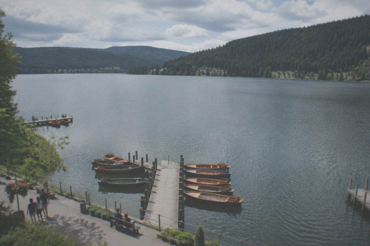 Calm forested lake with a wooden pier and wooded hills beyond on a clear summer morning