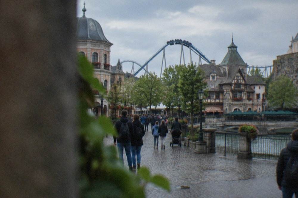 Wide view of a themed plaza at a large amusement park with visitors walking between decorated buildings
