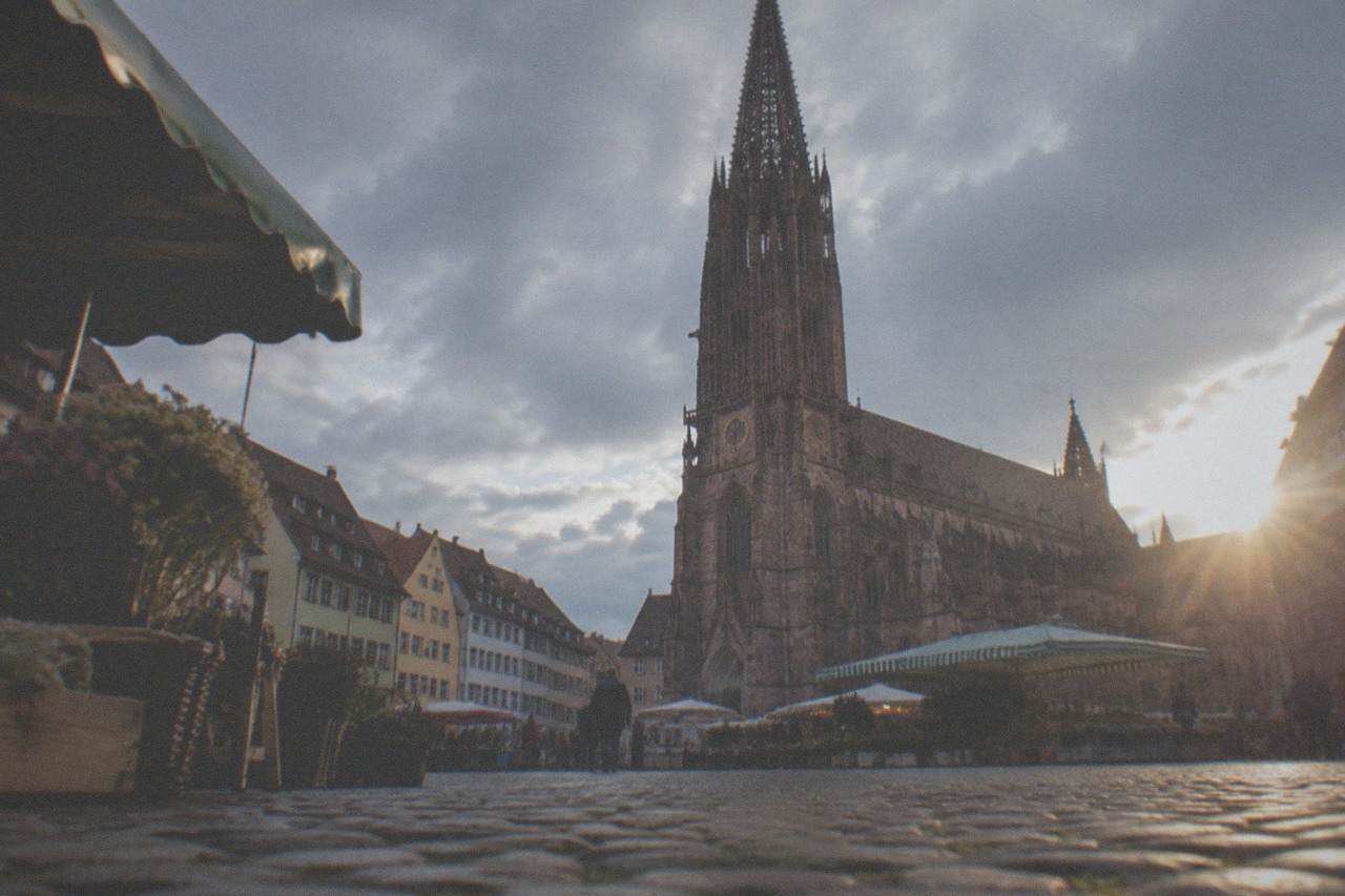 Cobblestone square in front of a Gothic red sandstone cathedral with market stalls and gabled town houses