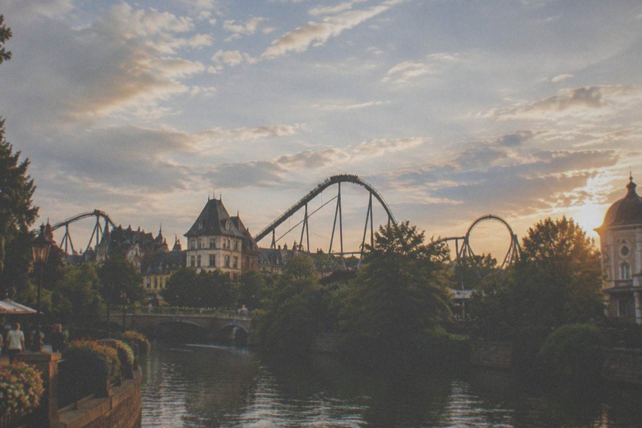 Roller coaster tracks rising above the tree line at a large theme park under a summer sky