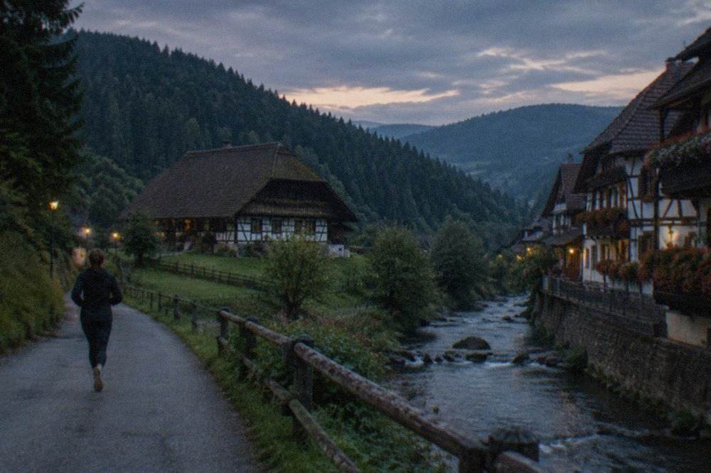 A half-timbered village street with geranium-covered balconies above a stream