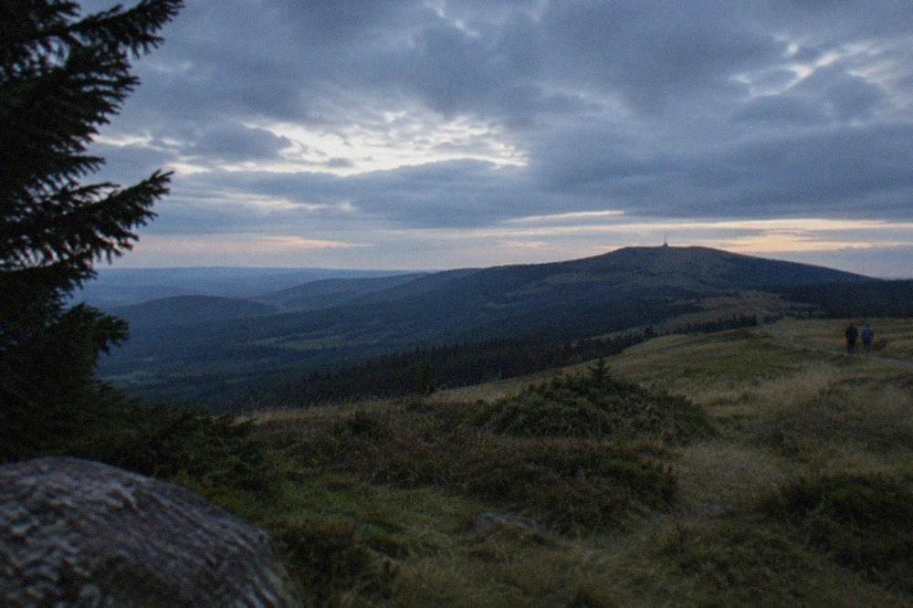Rolling forested hills rising toward a rounded grassy summit under a partly cloudy sky