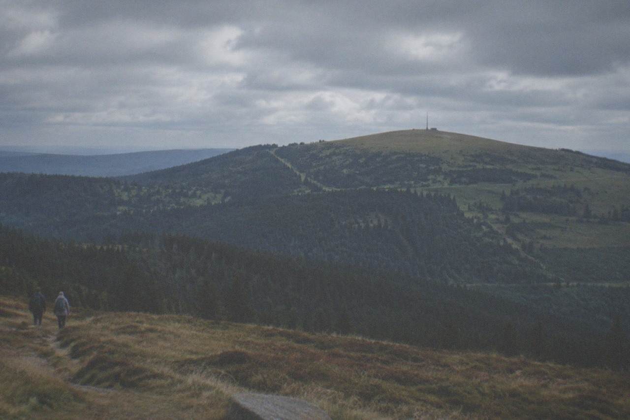 Rolling forested hills rising toward a rounded grassy summit under a partly cloudy sky
