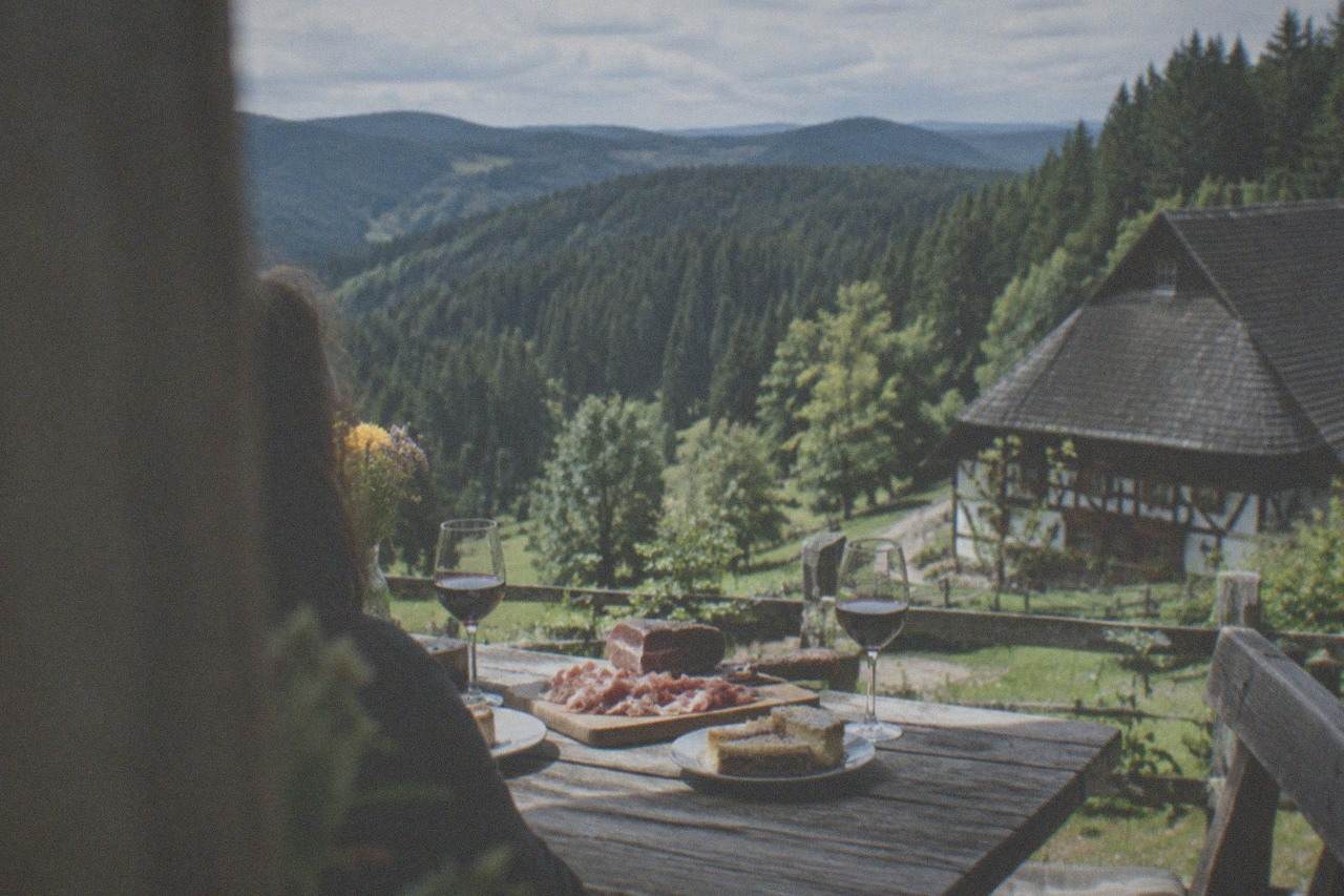 A rustic wooden table set with Black Forest ham, sliced cake and two glasses of red wine