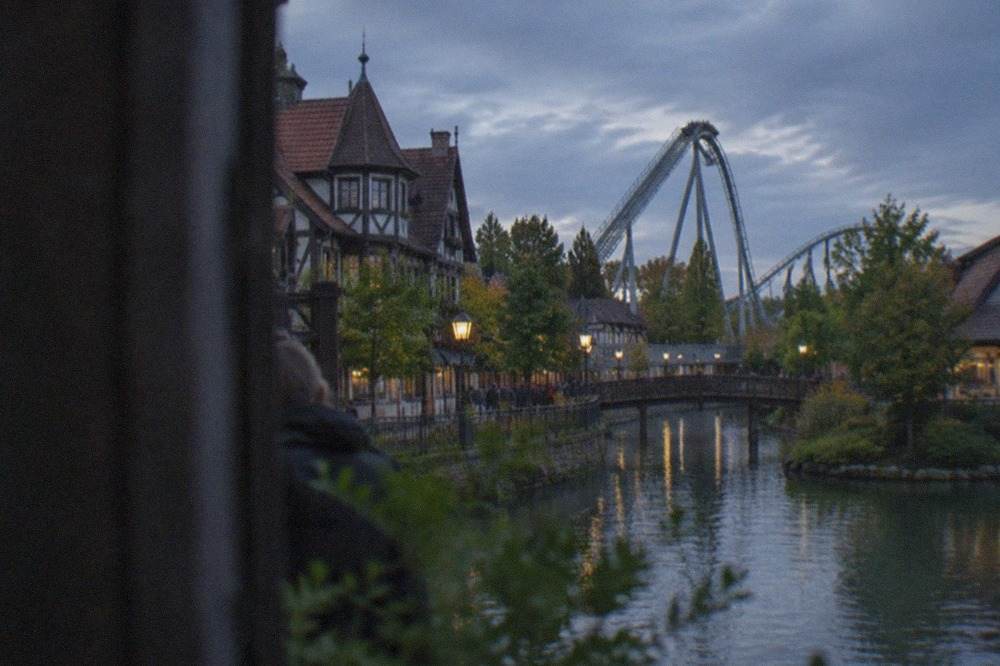 Wide view of a village street with half-timbered buildings and a tall coaster structure in the distance