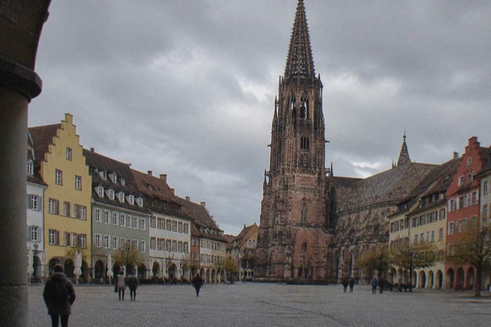 Cobblestone square with a gothic cathedral tower rising above rows of gabled old town houses