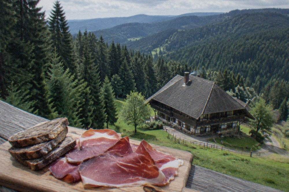 Slices of Black Forest ham arranged on a wooden board beside dark bread
