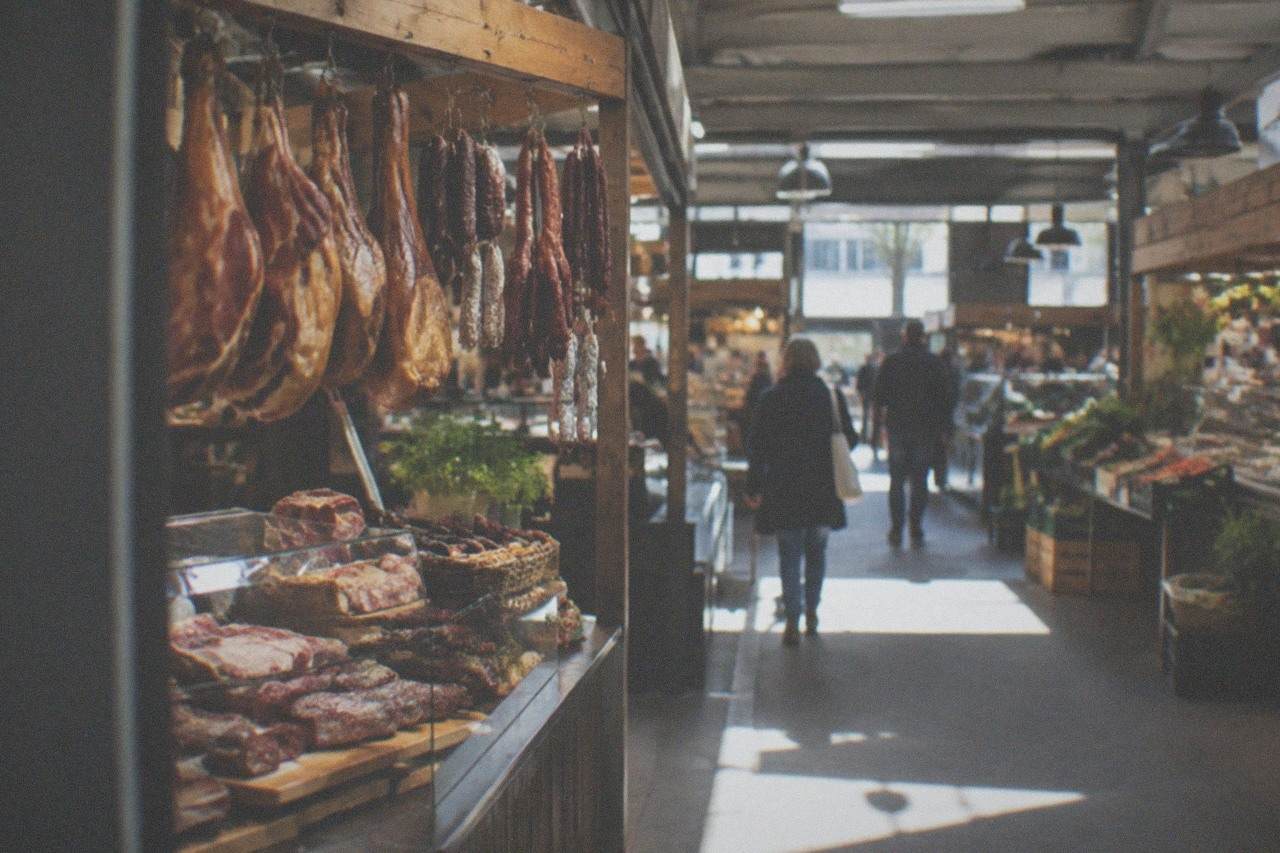 A market stall with smoked hams and regional sausages hanging under a wooden beam