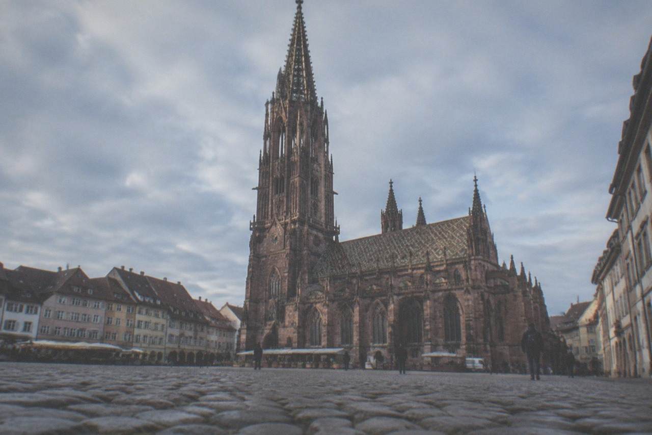 Cobbled market square in front of a tall red sandstone Gothic cathedral tower on a bright morning