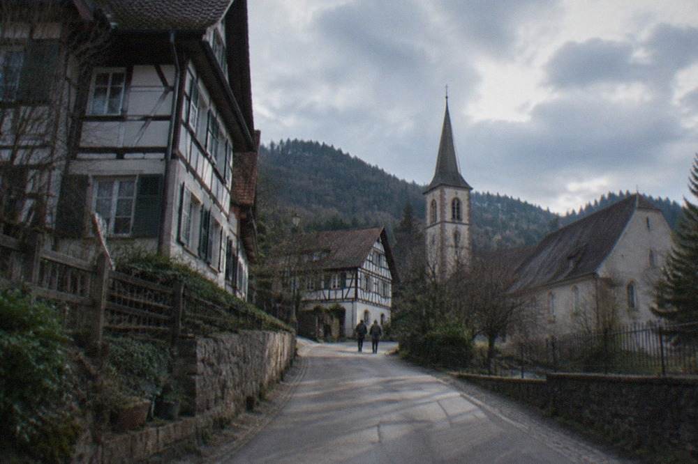 quiet street in Günterstal with old farmhouses, a church tower and forested hills behind