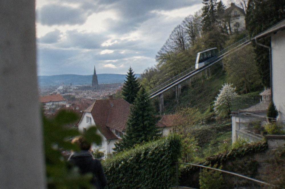 A modern inclined funicular lift rising along a wooded hillside above city rooftops