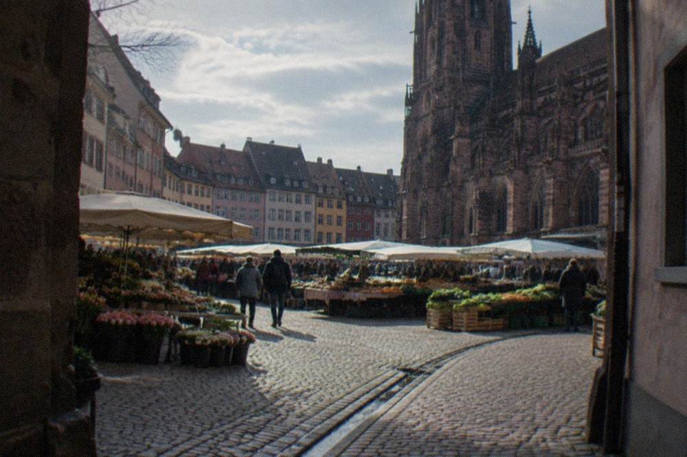 Market stalls with flowers, bread and vegetables spread across a cobbled cathedral square in the morning