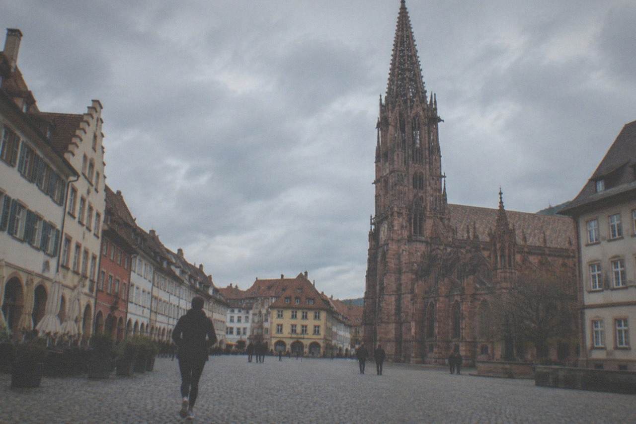 Cobbled square in Freiburg with historic guild houses and a Gothic cathedral tower rising above red rooftops