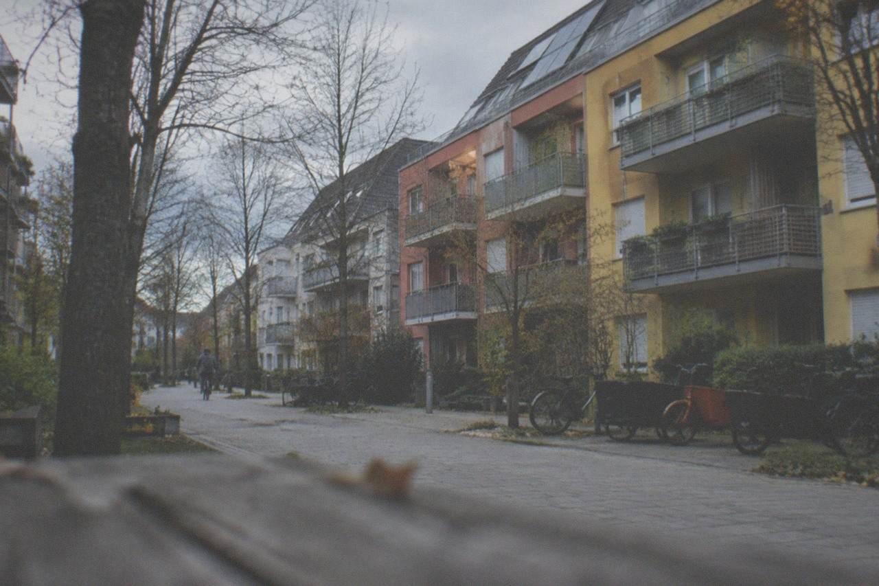 Row of colorful apartment buildings with balconies and trees along a quiet residential street