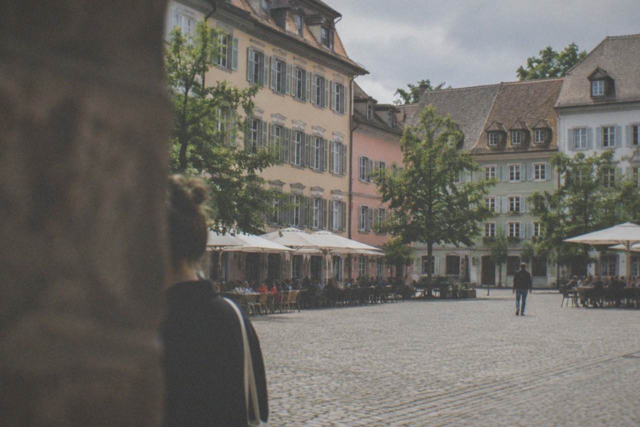 Cobblestone square with historic facades and café tables under trees on a warm evening