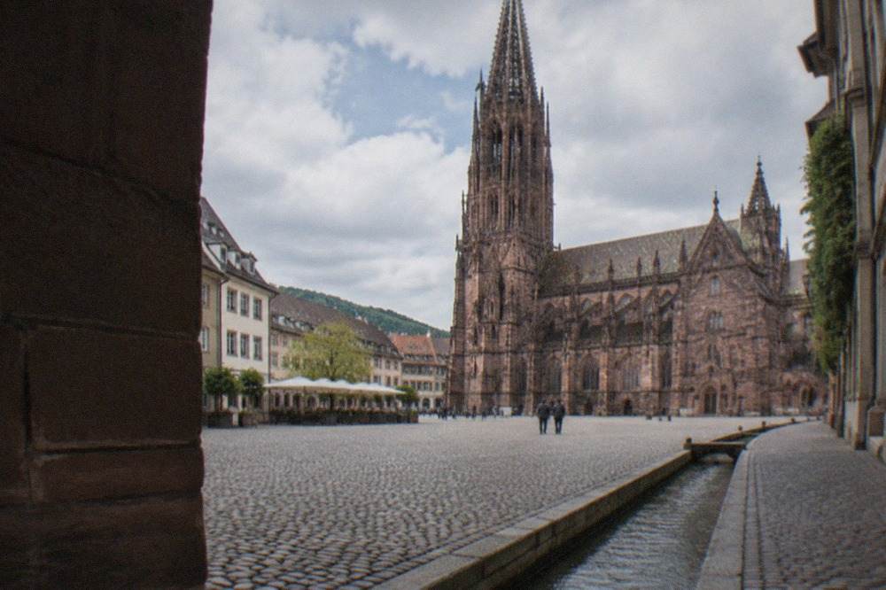 A narrow stone-lined water channel running beside the curb of a cobbled Freiburg street