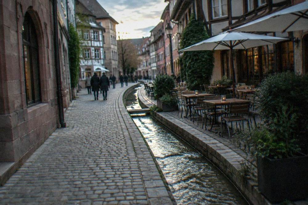 Evening light on an old town lane with a water channel running beside the pavement and a wine bar terrace