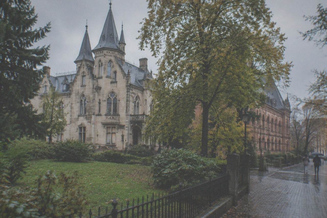 A small villa museum with an ornate brick facade standing behind trees on a quiet Freiburg street