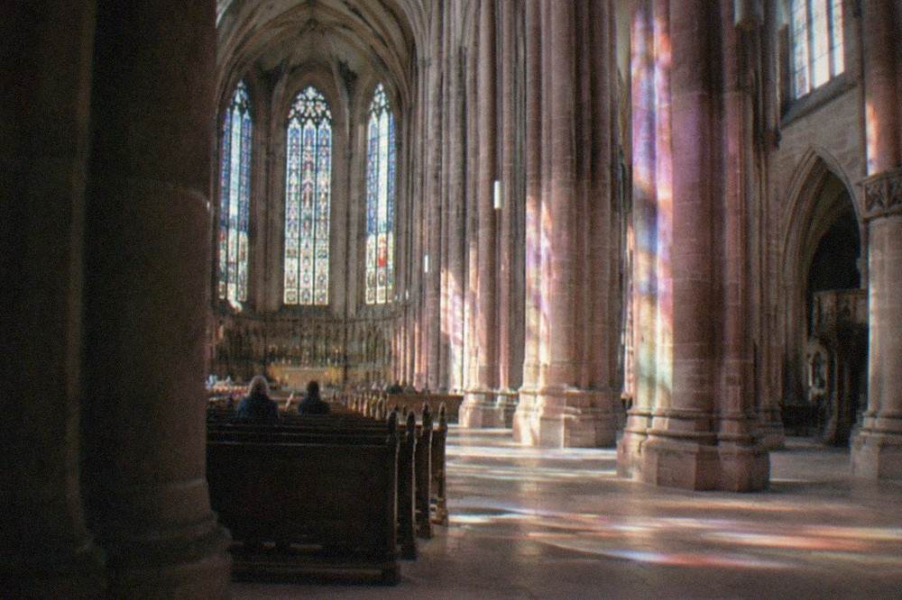 Interior of the minster nave with tall columns and colored light from choir windows