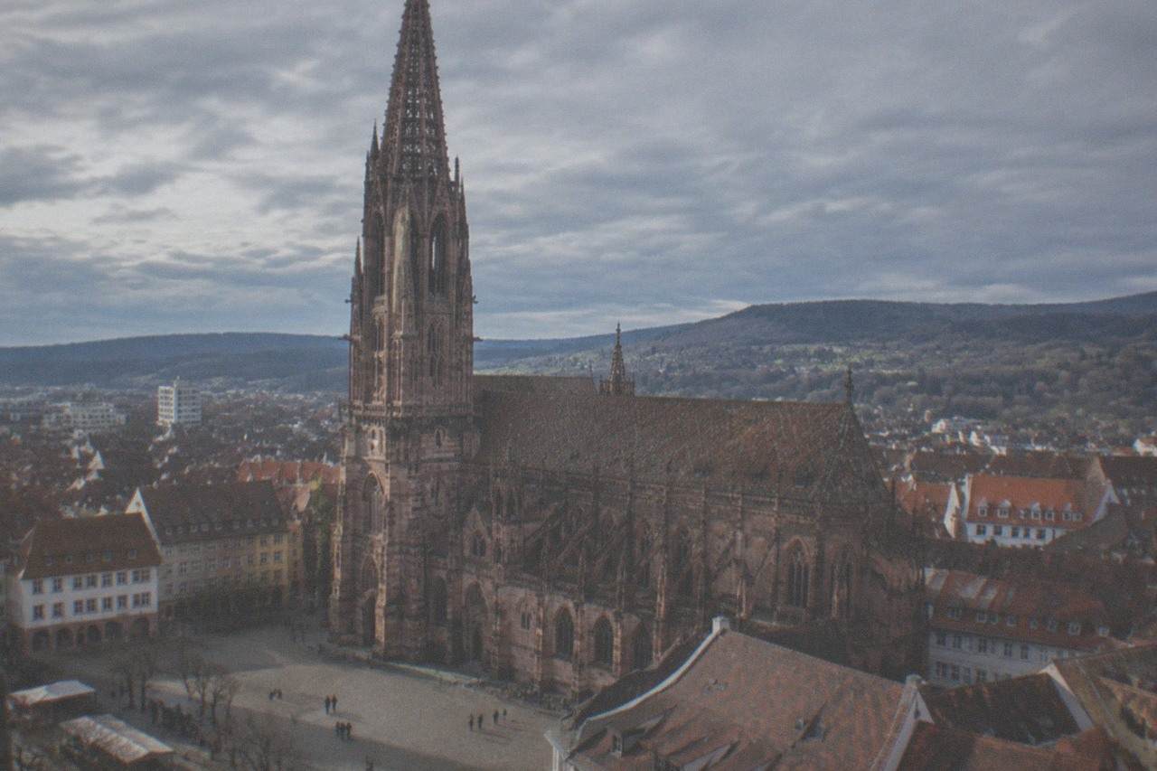 Gothic sandstone cathedral tower rising above red rooftops and a market square