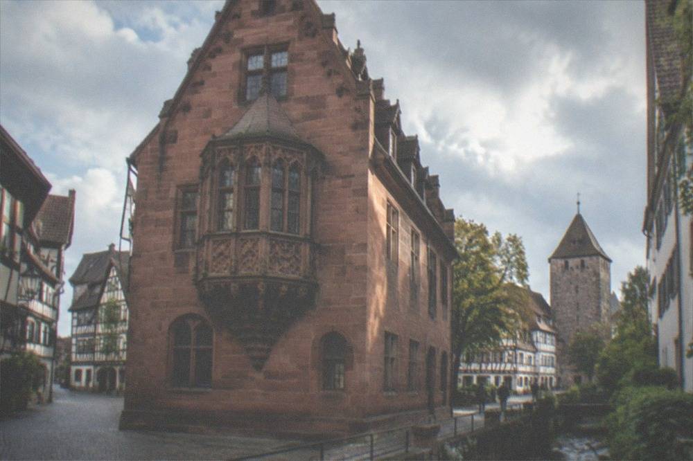 Old town street with small water channel, half-timbered houses and stone tower in the distance