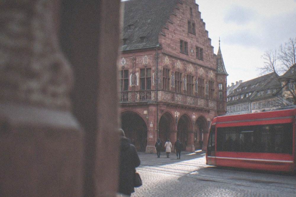 A red tram passing through a street at the edge of Freiburg's old town