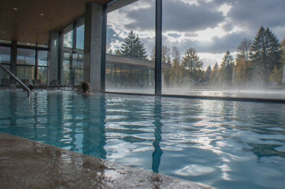 Indoor thermal pool with warm water and large windows looking out to trees