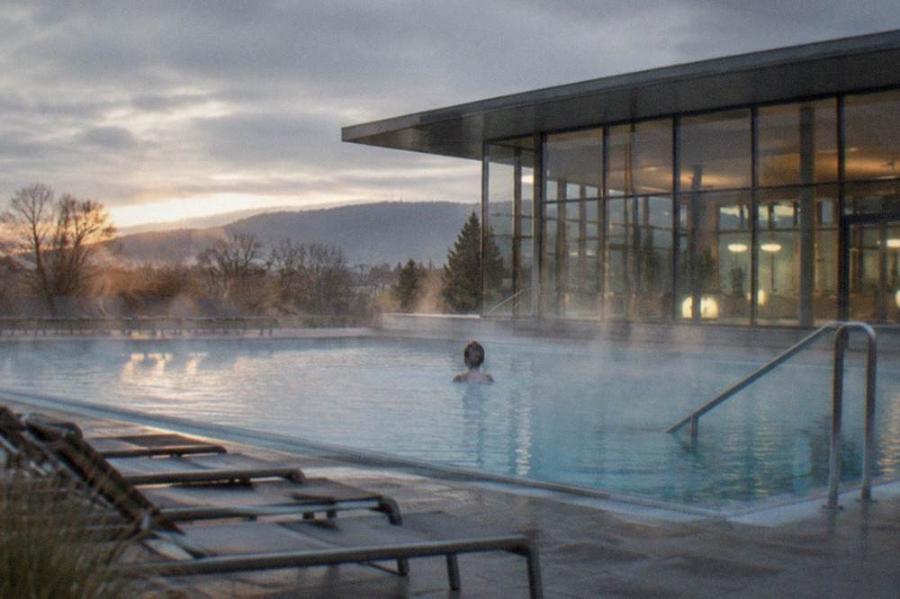 Outdoor thermal pool at dusk with steam rising and empty loungers along the edge