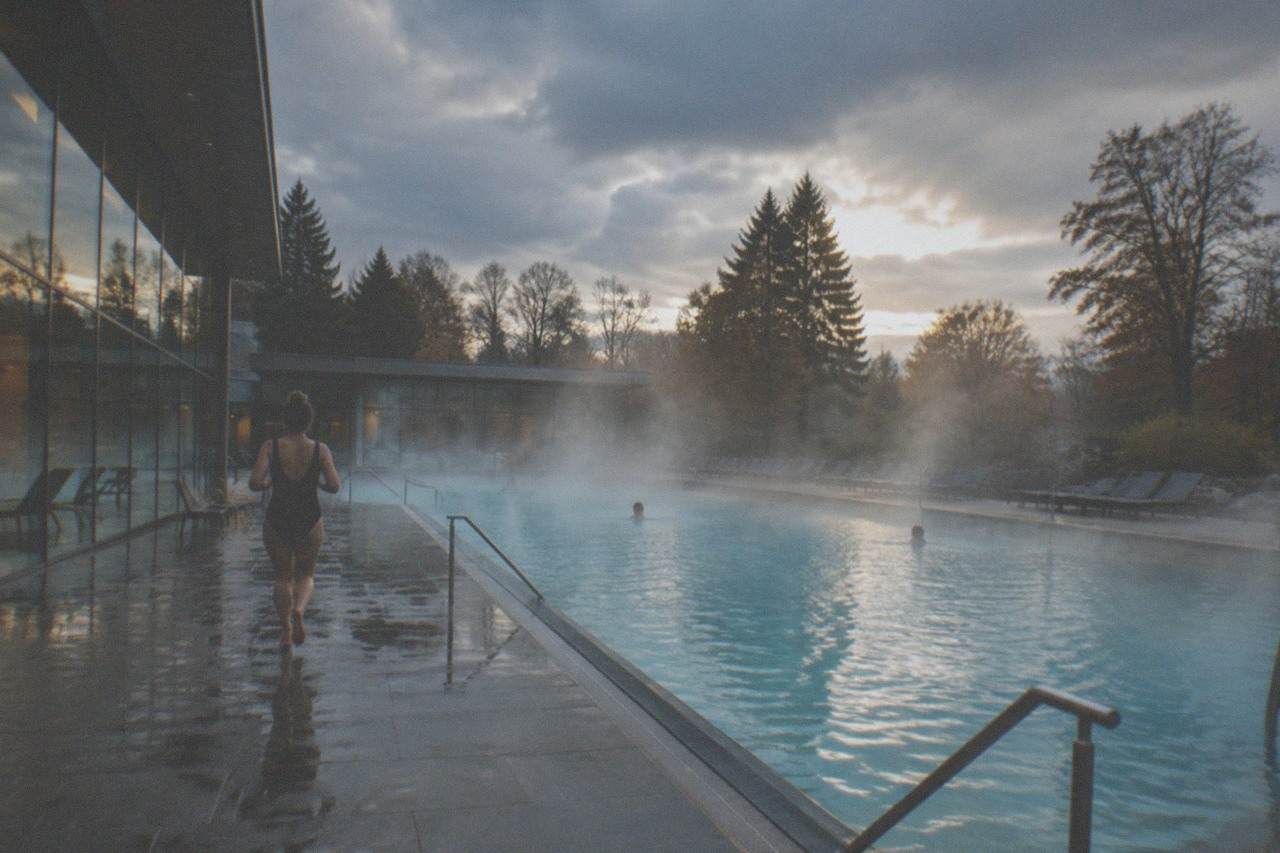 Steam rising from an outdoor thermal pool surrounded by trees on a cool evening