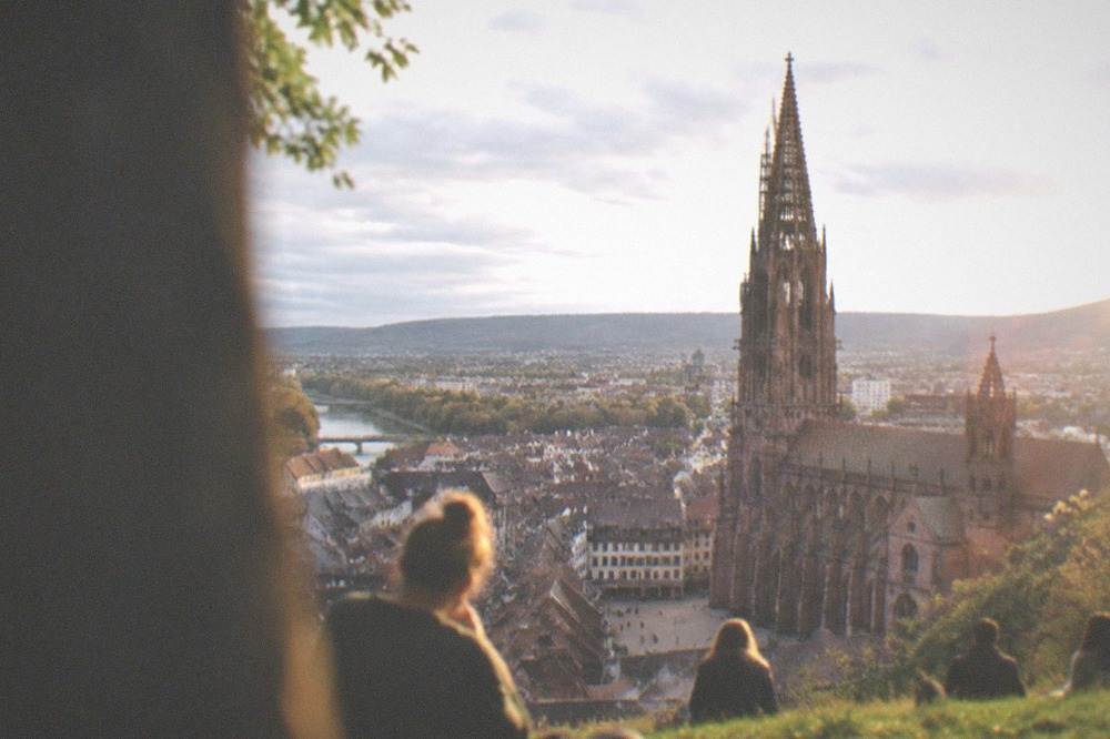 Visitors sitting on a grassy slope above Freiburg at golden hour with the city skyline below
