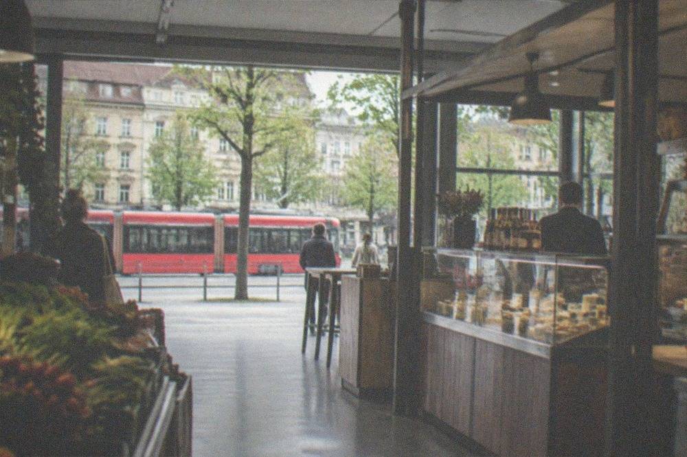 Red tram moving along a tree-lined street with old buildings behind