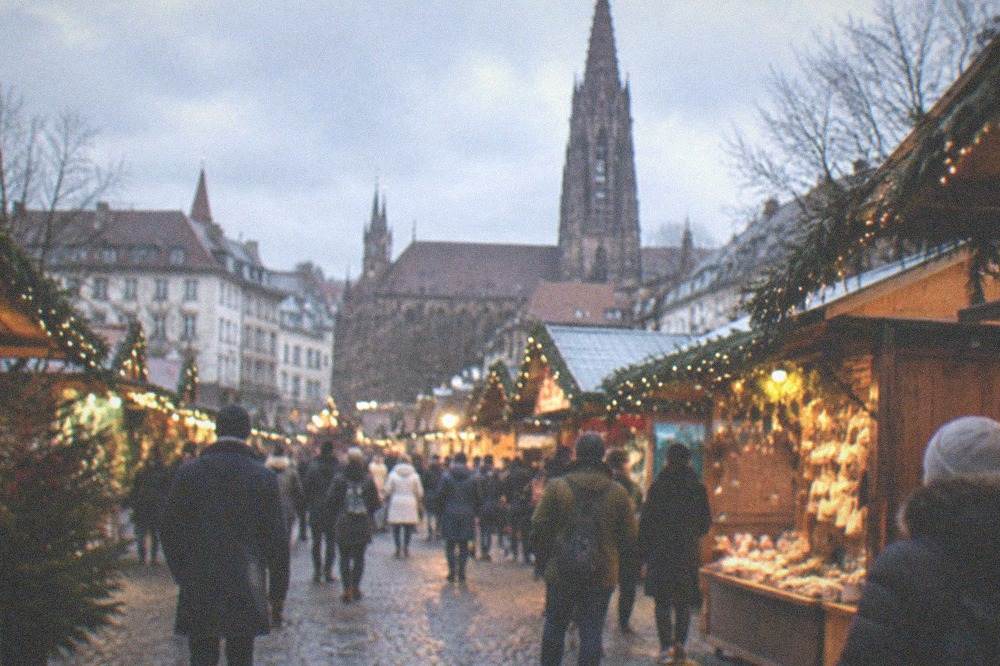 Old-town square at dusk with wooden Christmas market stalls and glowing lights