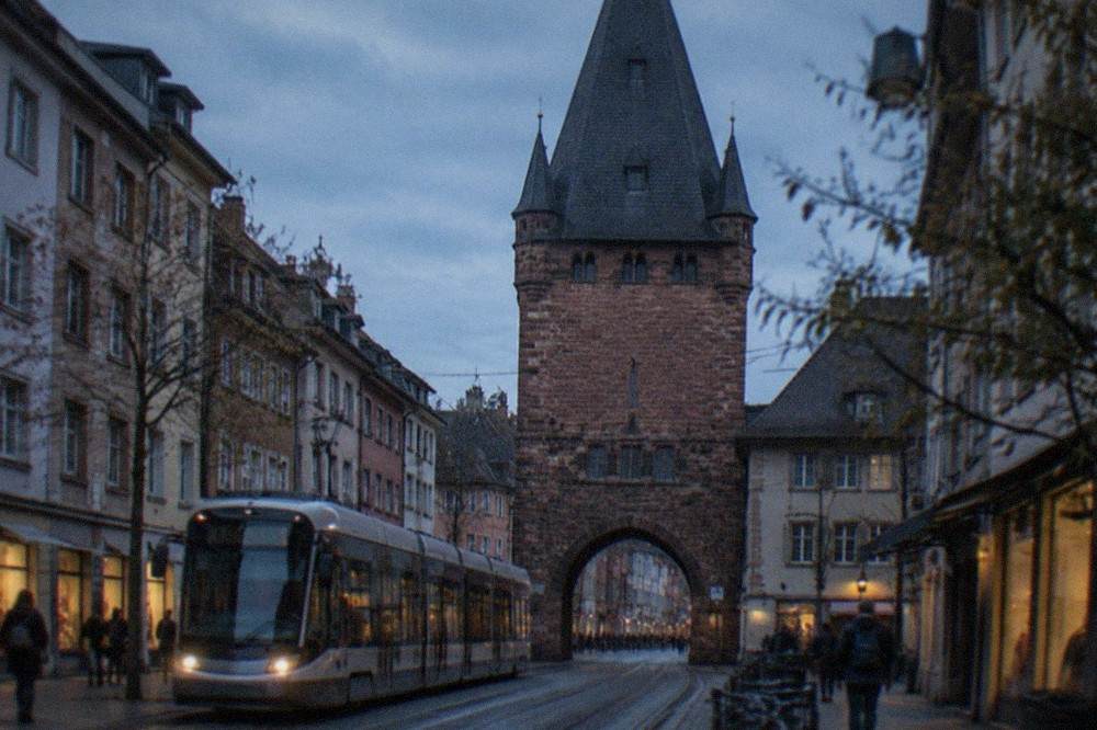 A modern tram passing through a city street with the old town lanes visible beyond