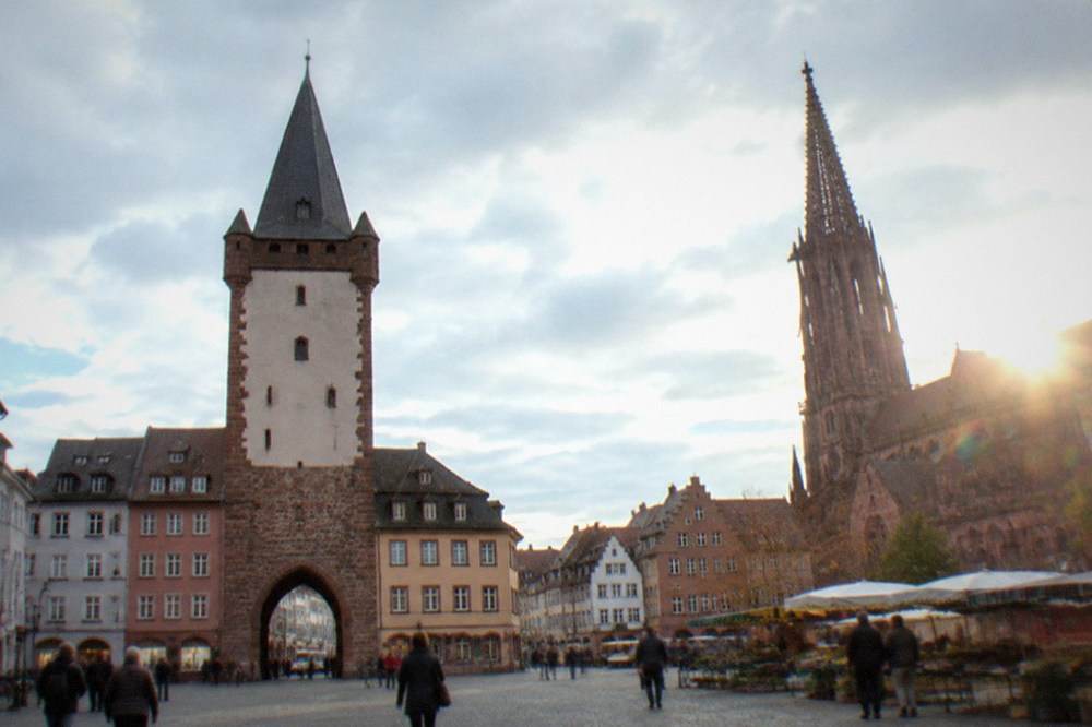 A busy cathedral square with a gothic spire, market stalls and historic merchant houses