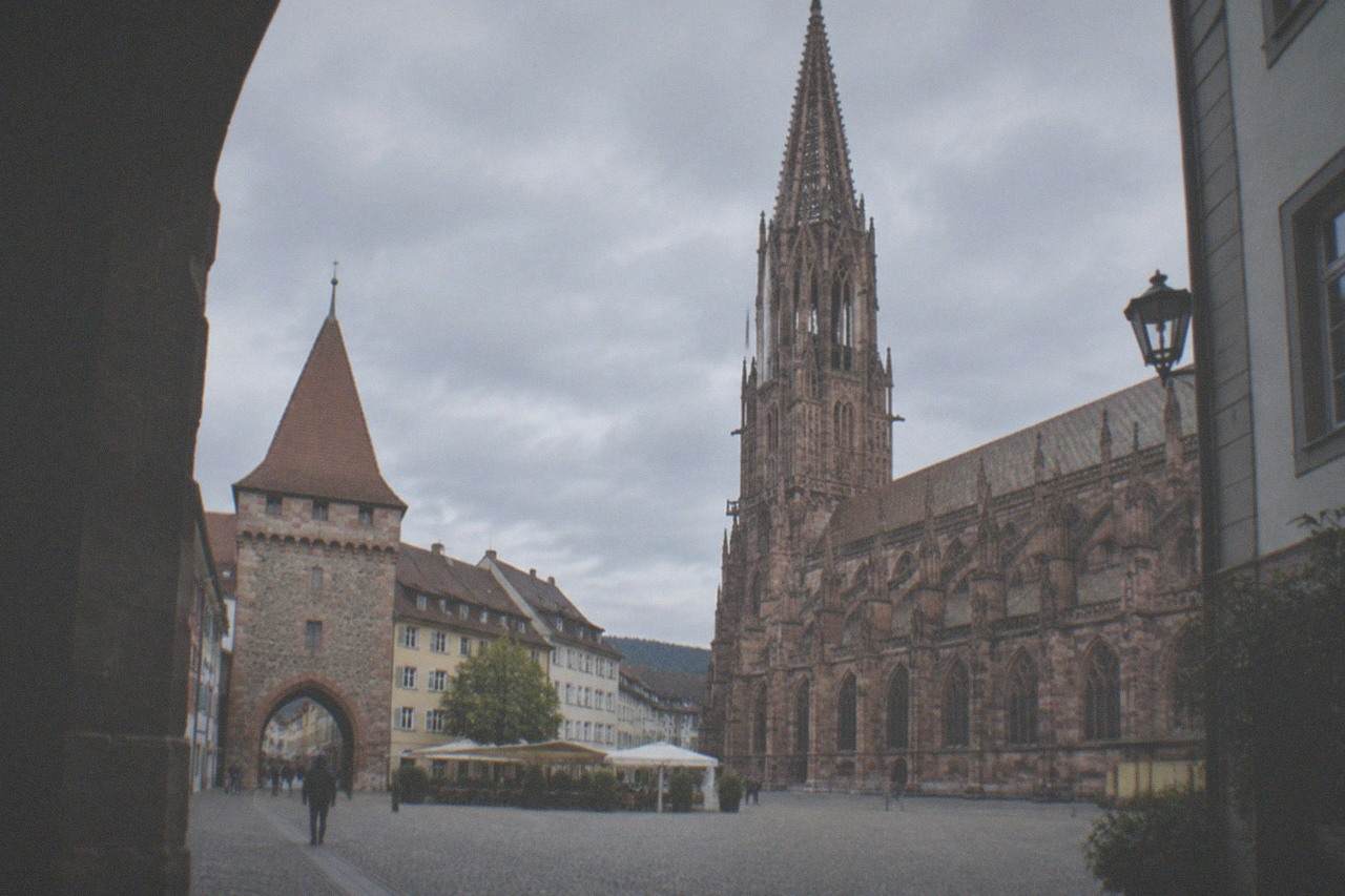 A stone medieval city gate with a pointed red roof standing over a pedestrian shopping street in Freiburg