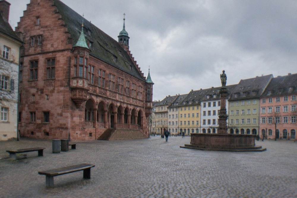 Cobbled civic square with a historic facade and empty benches in morning light