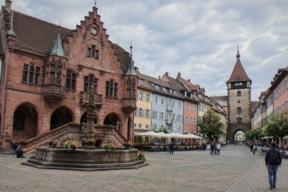 Narrow old town lane with pastel facades leading toward a medieval gate tower