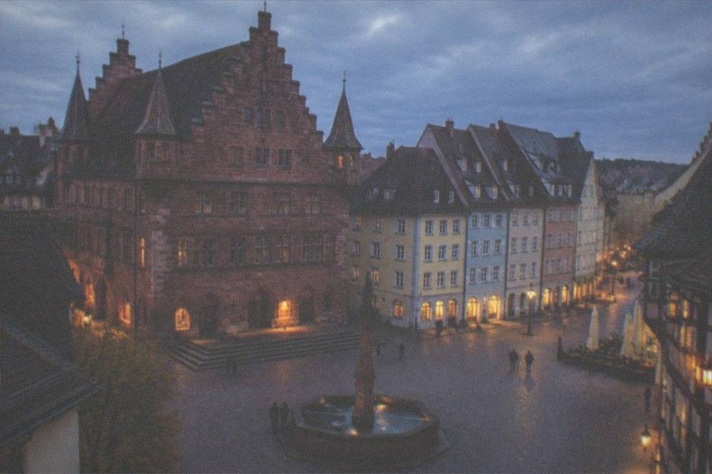 Old town street corner at dusk with warm lamplight on dark timbered facades