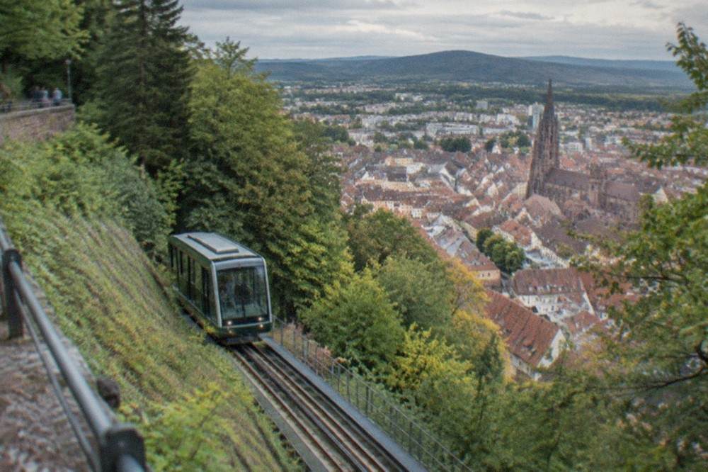 Inclined funicular railway car climbing a steep green hillside above city rooftops