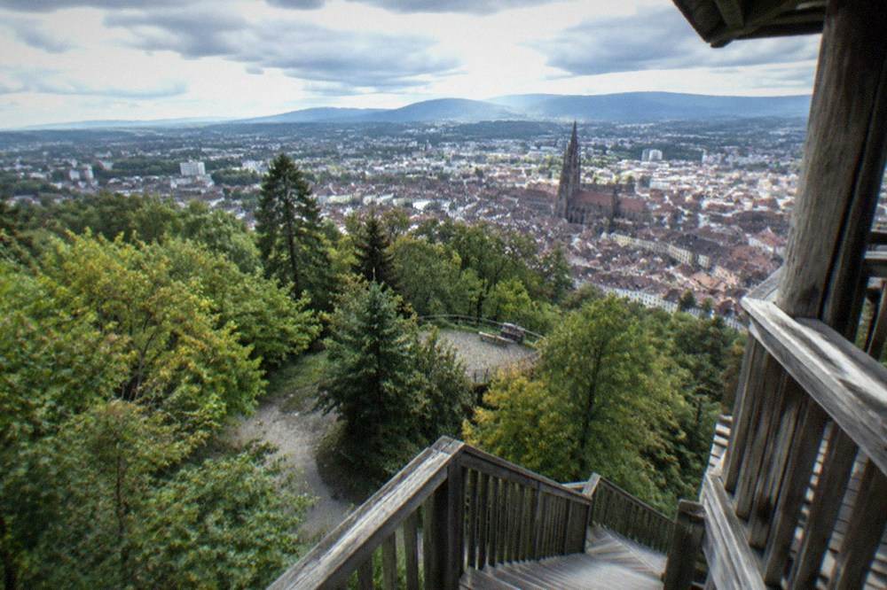 Wooden staircase platform inside an open lookout tower with panoramic views over a city and distant mountains