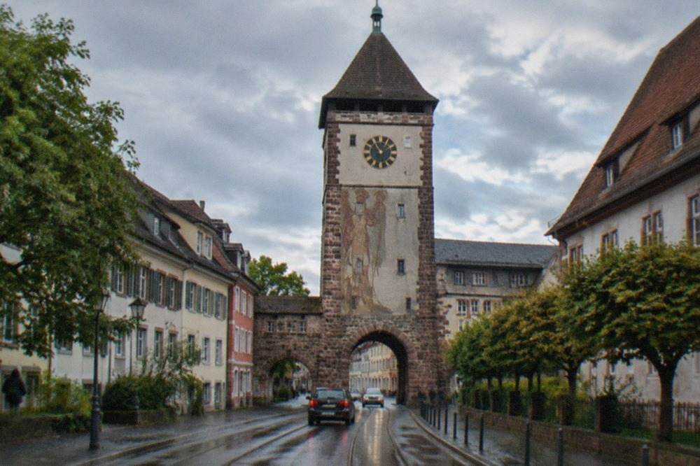 The stone gate tower with its clock face seen along a narrow street