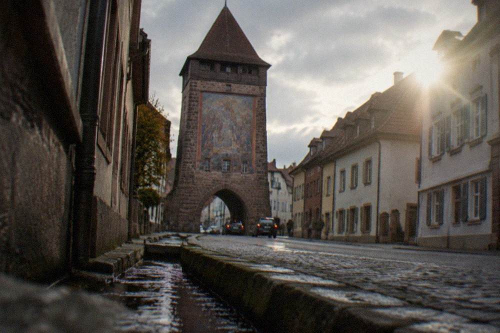 Narrow old town street with a water channel along the kerb leading toward the gate tower