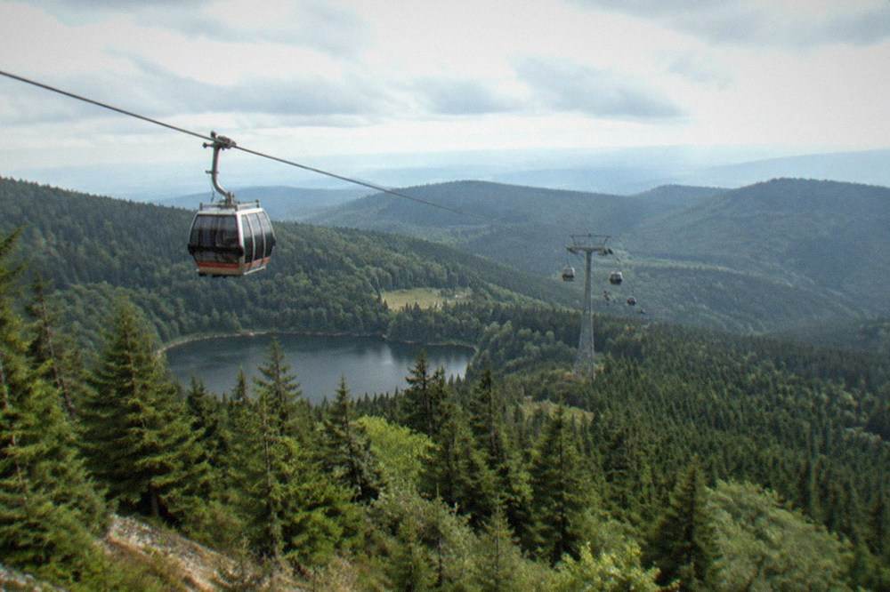 A cable car cabin suspended above dense green forest on a mountainside.