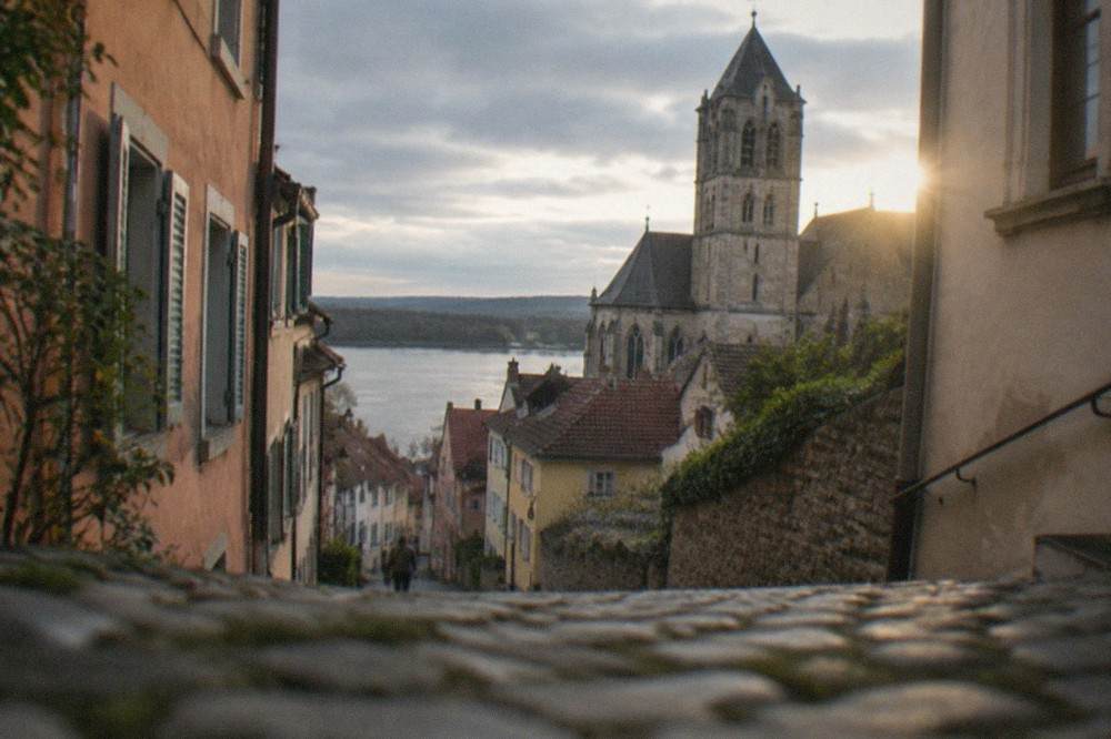Narrow cobblestone lane climbing between tall painted town houses toward a stone church tower