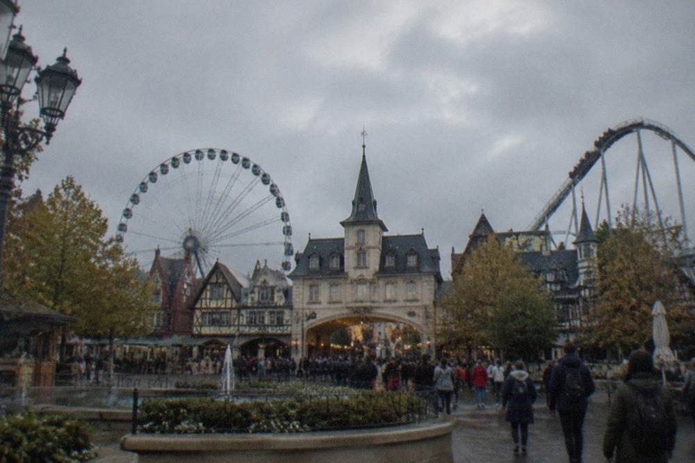 Theme park entrance plaza with a European village facade and a ferris wheel in the background