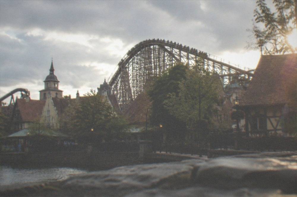 Wooden roller coaster structure rising above themed European village rooftops in a theme park