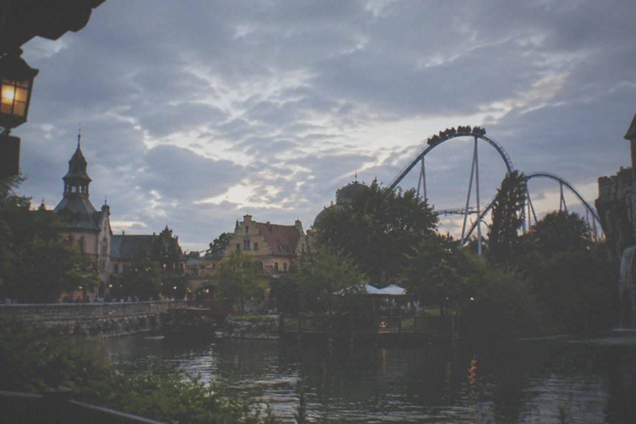 Roller coaster track curving over a European-themed park skyline under a summer sky