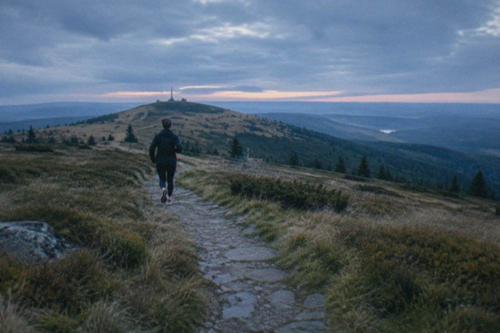 Wide upland meadow with a stone path leading toward a rounded summit under scattered clouds