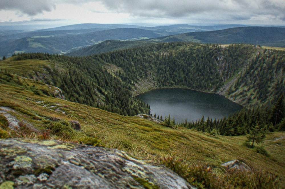Small dark lake ringed by steep forested slopes at the bottom of a rocky cirque