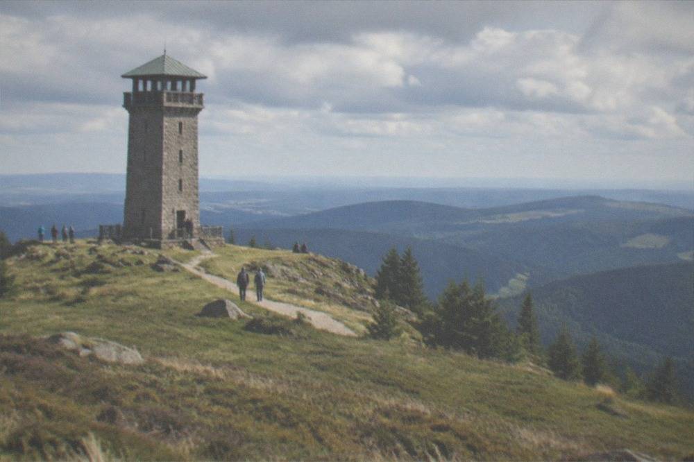 Stone lookout tower on a grassy ridge with layered hills fading into blue haze on the horizon